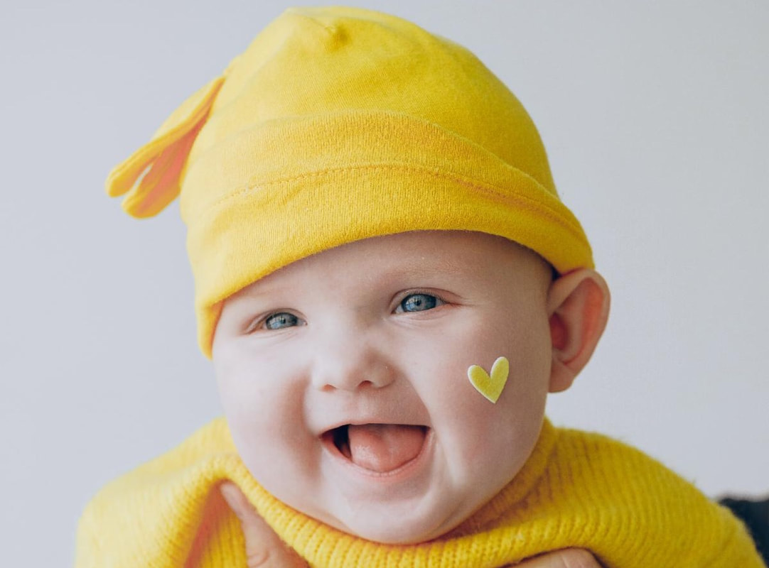 Baby wearing a yellow hat and sweater, smiling.